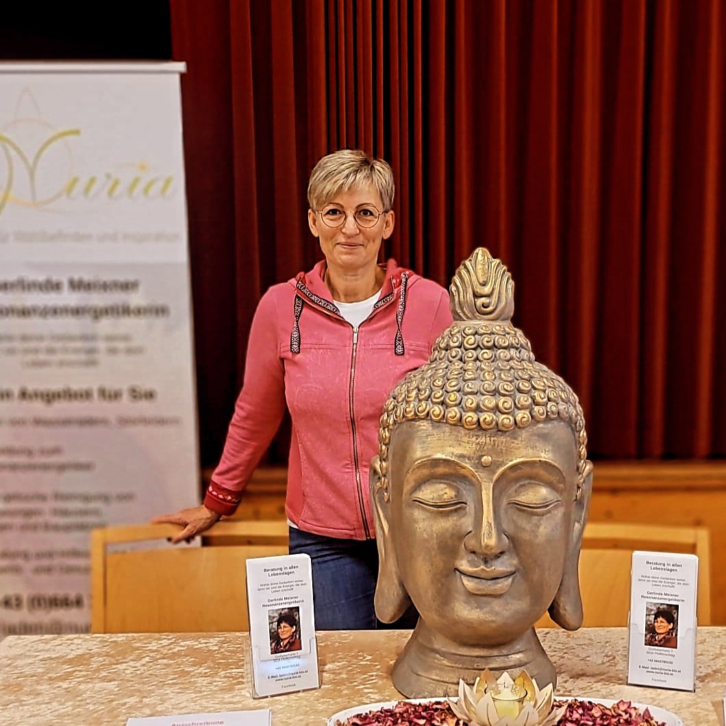 Gerlinde Meixner mit rosa Weste an ihrem Ausstellungsstand mit goldener Statue und Flyern